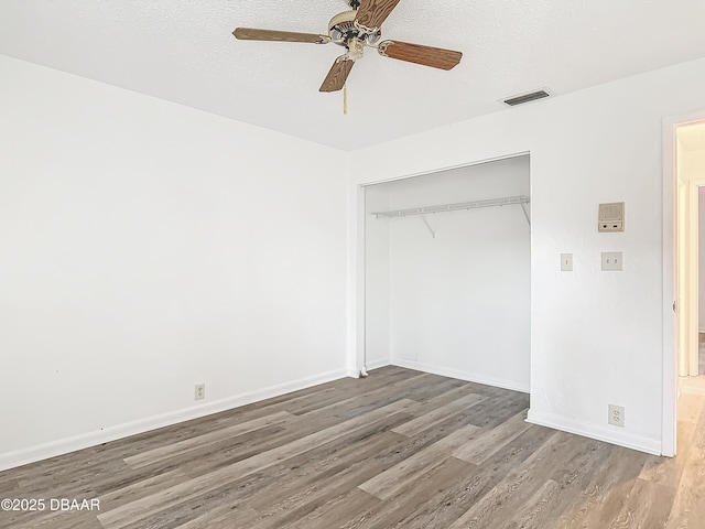 unfurnished bedroom with a closet, visible vents, a textured ceiling, wood finished floors, and baseboards