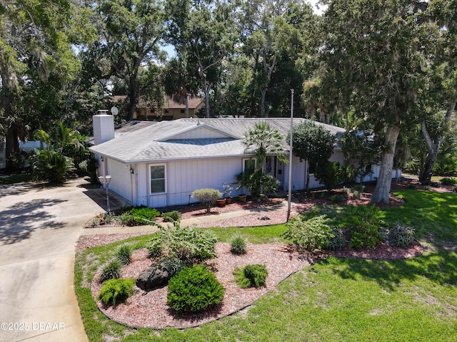 view of front of house with a front yard, roof with shingles, driveway, and a chimney