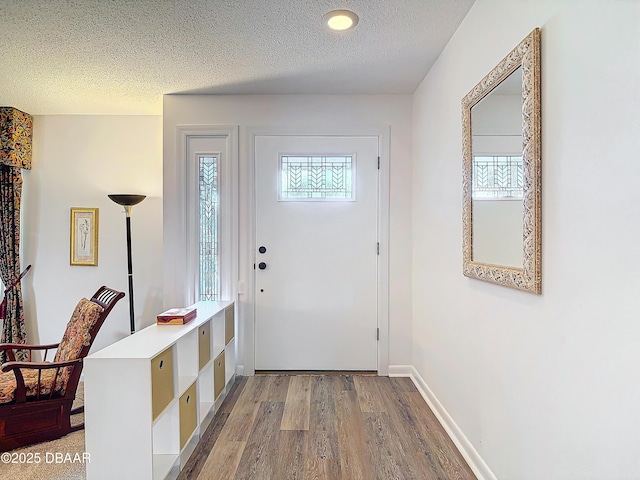 doorway to outside featuring a textured ceiling, baseboards, and wood finished floors