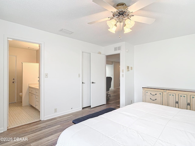 bedroom with a textured ceiling, visible vents, wood finished floors, and ensuite bathroom