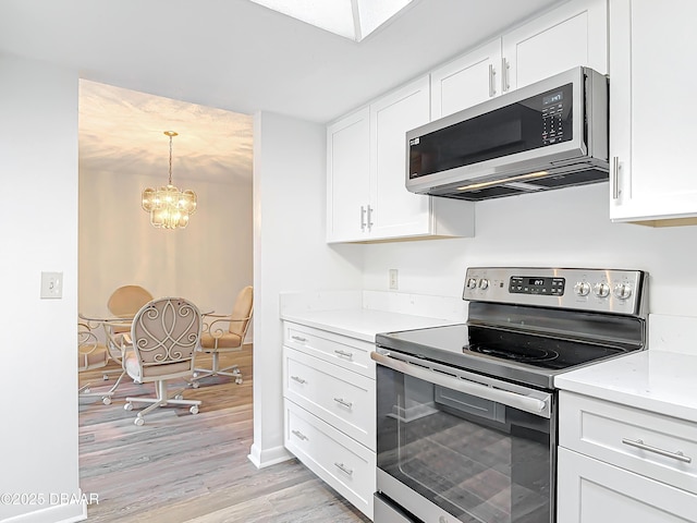 kitchen with decorative light fixtures, appliances with stainless steel finishes, light wood-style floors, white cabinetry, and light stone countertops