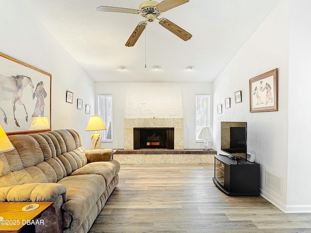 living area featuring a fireplace, visible vents, light wood-style floors, ceiling fan, and a textured ceiling