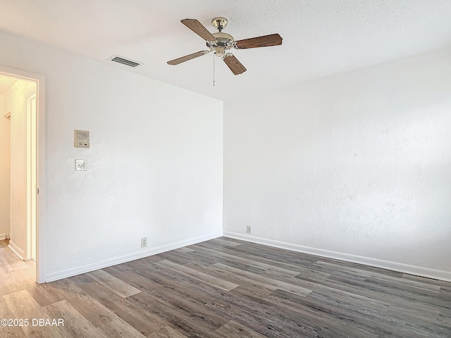 spare room with dark wood-type flooring, a ceiling fan, visible vents, and baseboards