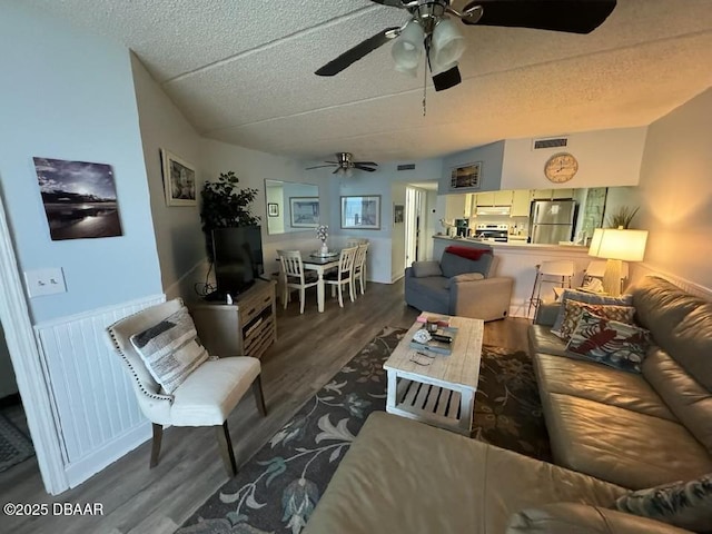 living area with wainscoting, wood finished floors, visible vents, and a textured ceiling