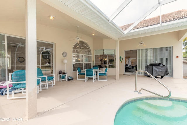 view of pool featuring a patio, glass enclosure, ceiling fan, and grilling area