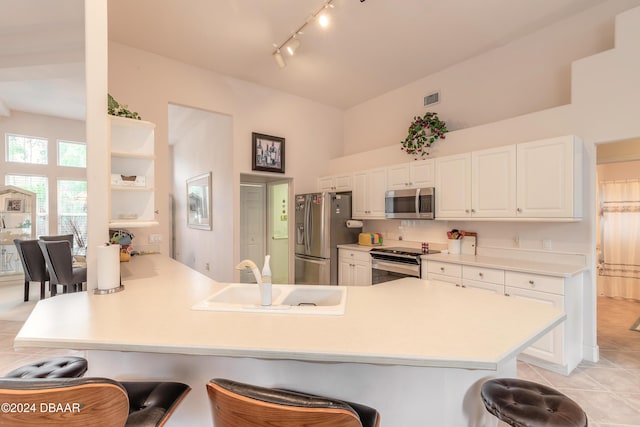 kitchen featuring kitchen peninsula, appliances with stainless steel finishes, sink, light tile patterned floors, and a breakfast bar area