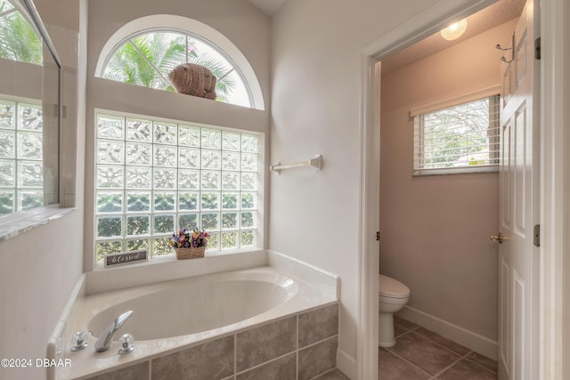 bathroom featuring tiled bath, a healthy amount of sunlight, and toilet