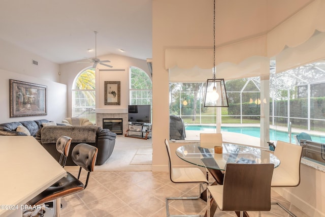 tiled dining area with a tiled fireplace, ceiling fan, and vaulted ceiling