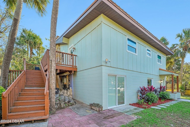 back of property featuring stairway, board and batten siding, a deck, and a patio