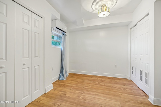 unfurnished bedroom with a wall mounted AC, light hardwood / wood-style flooring, and two closets