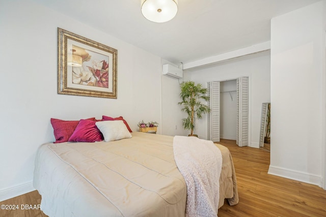 bedroom with a wall unit AC, light wood-style flooring, baseboards, and a closet