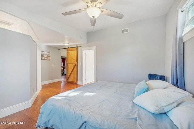 bedroom with visible vents, a ceiling fan, wood finished floors, a barn door, and baseboards