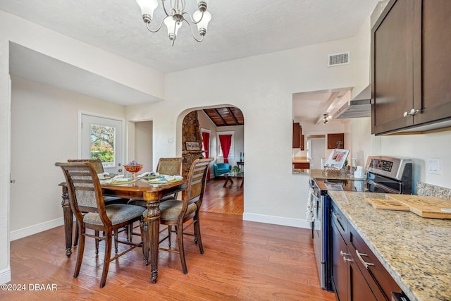 dining room featuring visible vents, arched walkways, baseboards, and light wood finished floors