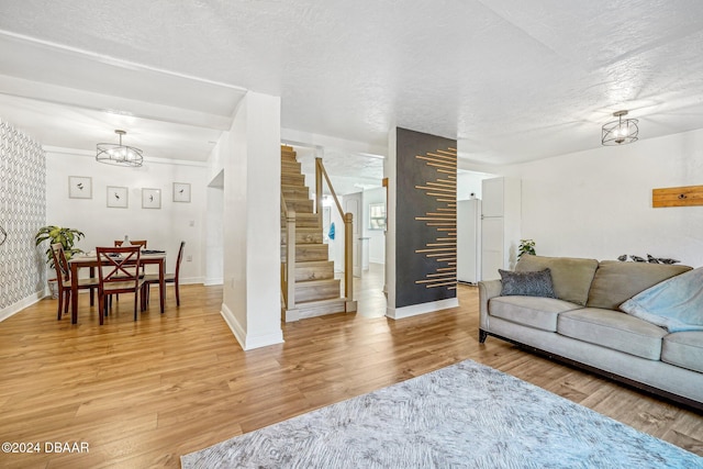 living room with light wood-style flooring, a textured ceiling, stairs, and baseboards