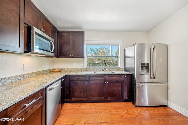 kitchen featuring light wood-type flooring, appliances with stainless steel finishes, sink, and light stone counters