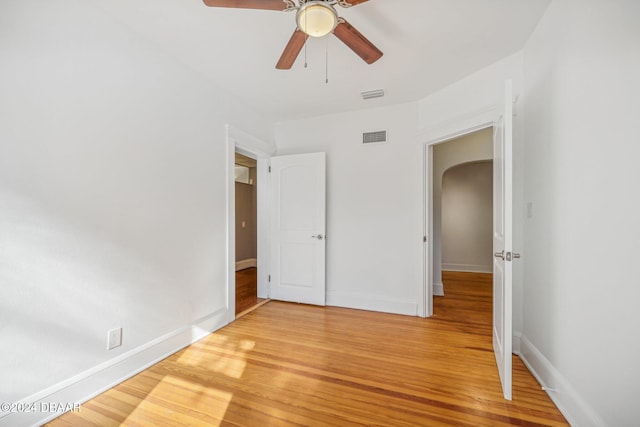 unfurnished bedroom featuring light wood finished floors, visible vents, baseboards, arched walkways, and a ceiling fan