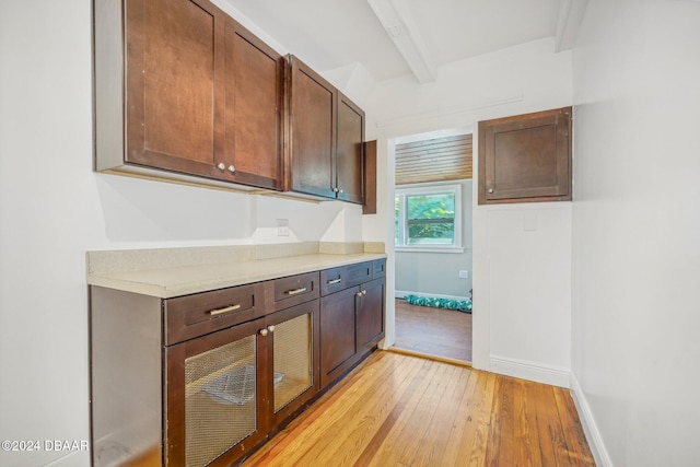 kitchen with baseboards, dark brown cabinetry, light countertops, beam ceiling, and light wood-style flooring