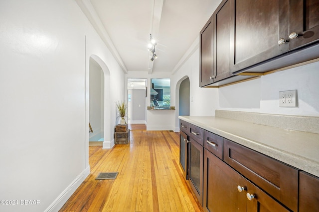 corridor featuring light wood-type flooring, visible vents, track lighting, arched walkways, and baseboards