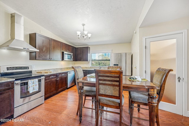 kitchen with dark brown cabinets, wall chimney exhaust hood, light hardwood / wood-style floors, and appliances with stainless steel finishes