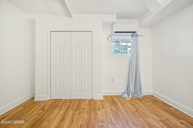 unfurnished bedroom with an AC wall unit, light wood-style flooring, baseboards, and a closet