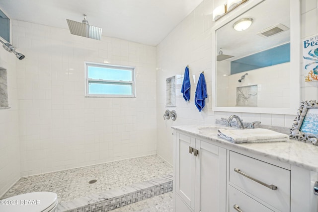 bathroom with visible vents, toilet, vanity, and tiled shower