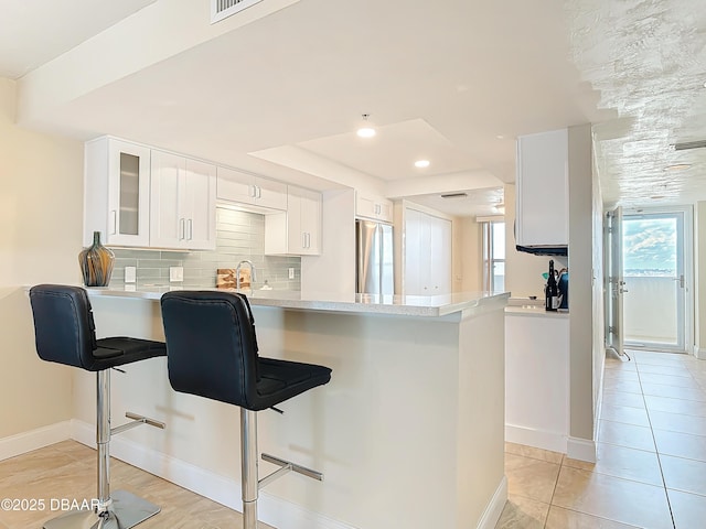 3333 S Atlantic Ave Unit 505, Daytona Beach, FL 32118 - kitchen featuring stainless steel fridge, a peninsula, light countertops, a raised ceiling, and glass insert cabinets