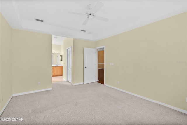 unfurnished bedroom with ceiling fan, ensuite bathroom, a tray ceiling, and light carpet