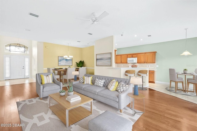 living room featuring ceiling fan with notable chandelier and light hardwood / wood-style flooring