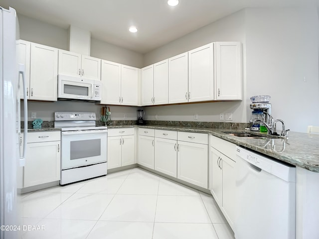 kitchen featuring white appliances, dark stone counters, sink, light tile patterned floors, and white cabinetry