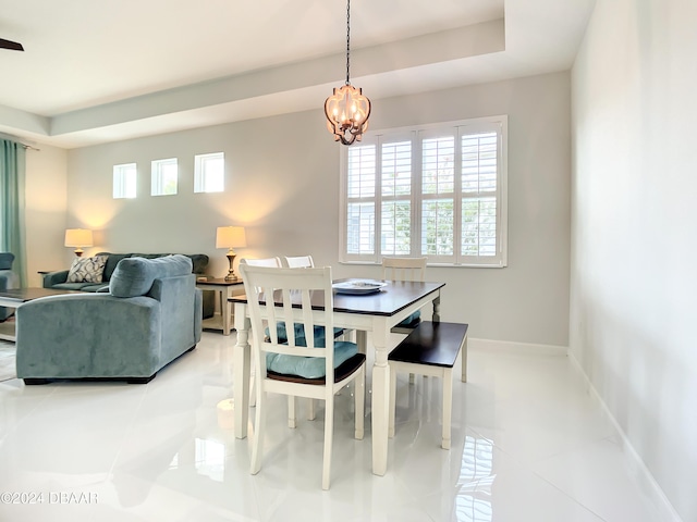 tiled dining space with a raised ceiling and a notable chandelier