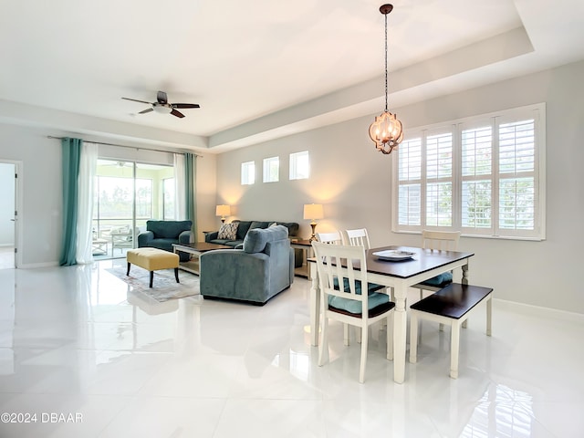 tiled dining room featuring a tray ceiling and ceiling fan with notable chandelier