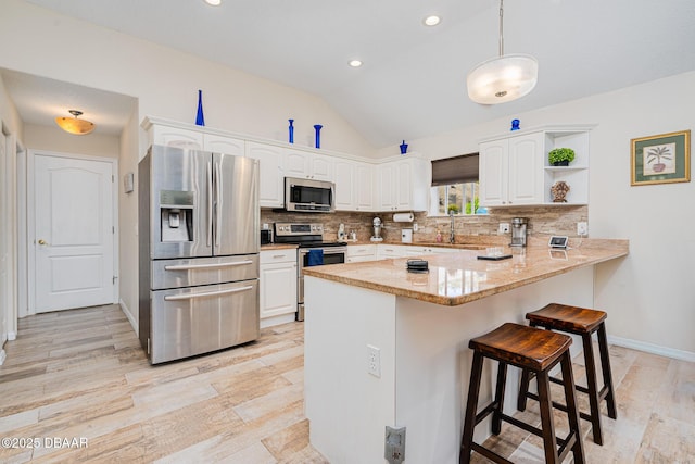 kitchen with white cabinets, a peninsula, a sink, lofted ceiling, and appliances with stainless steel finishes