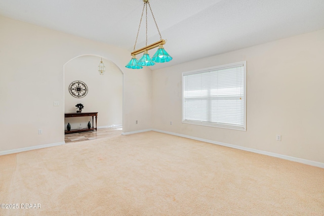 spare room featuring arched walkways, light carpet, and baseboards