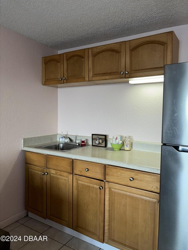 3501 S Atlantic Ave E Unit G20, Daytona Beach Shores, FL 32118 - kitchen with freestanding refrigerator, light countertops, a textured ceiling, brown cabinets, and light tile patterned floors