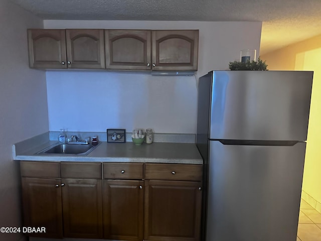 kitchen featuring stainless steel fridge, dark brown cabinetry, light tile patterned floors, and sink