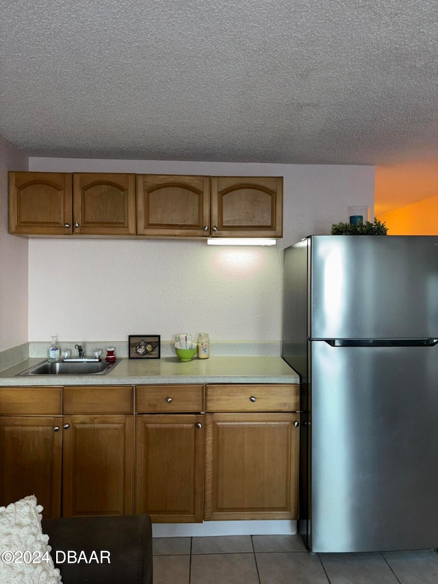 kitchen with light tile patterned flooring, stainless steel fridge, a textured ceiling, and sink