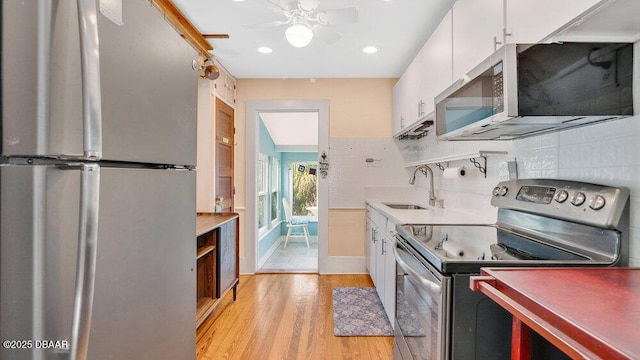 kitchen featuring sink, white cabinetry, stainless steel appliances, light hardwood / wood-style floors, and backsplash