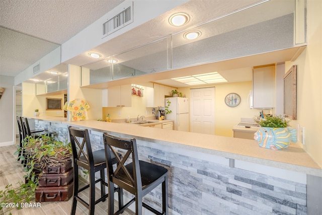 kitchen featuring white cabinetry, a kitchen breakfast bar, white refrigerator, and light hardwood / wood-style floors