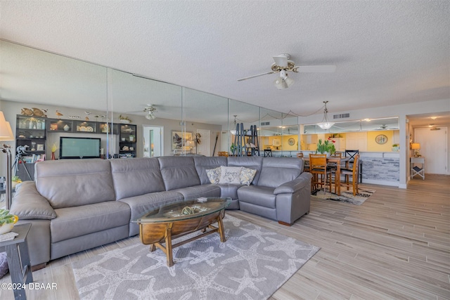 living room with ceiling fan, a textured ceiling, and light wood-type flooring