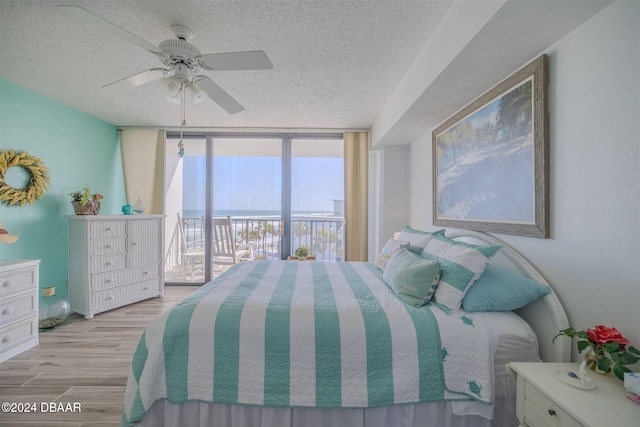 bedroom featuring a water view, floor to ceiling windows, ceiling fan, access to exterior, and light wood-type flooring