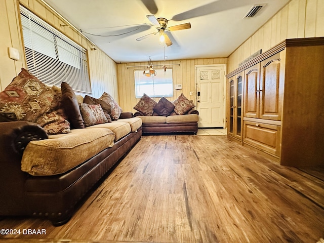 living room with light wood-type flooring, ceiling fan, and wooden walls