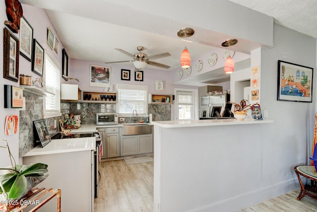 kitchen featuring pendant lighting, sink, stainless steel appliances, kitchen peninsula, and light wood-type flooring