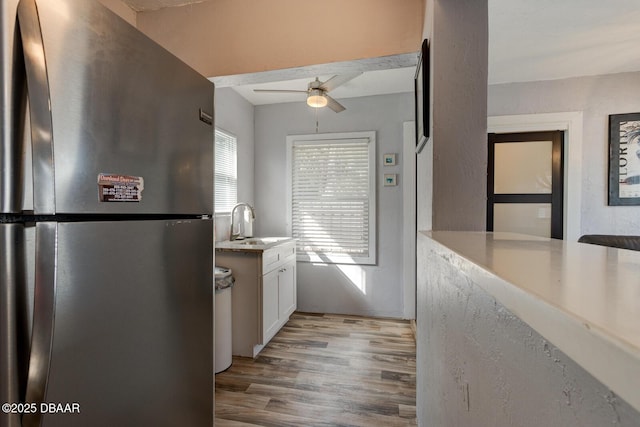 kitchen with sink, stainless steel refrigerator, ceiling fan, white cabinets, and light wood-type flooring