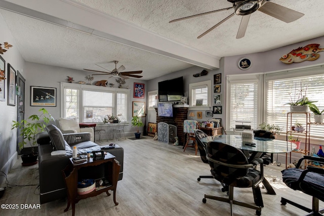 interior space with a fireplace, beamed ceiling, ceiling fan, light hardwood / wood-style floors, and a textured ceiling