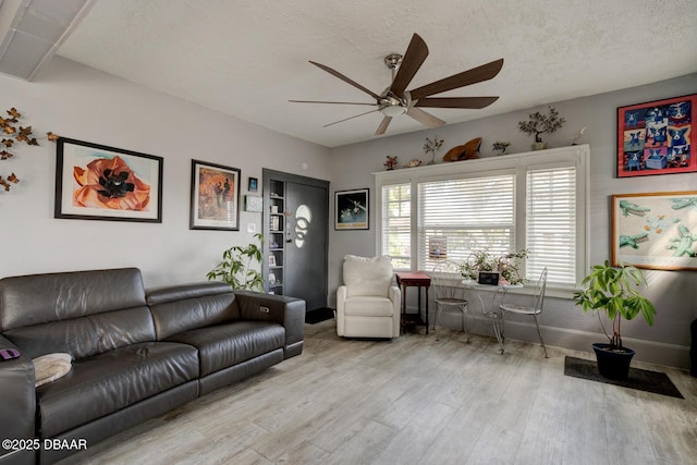 living room with ceiling fan, a textured ceiling, and light hardwood / wood-style flooring