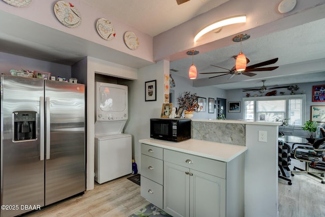 kitchen with light hardwood / wood-style flooring, stainless steel fridge, stacked washing maching and dryer, a textured ceiling, and kitchen peninsula