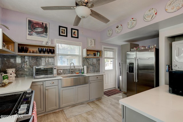 kitchen with sink, gray cabinetry, stacked washer / dryer, stainless steel appliances, and light hardwood / wood-style floors