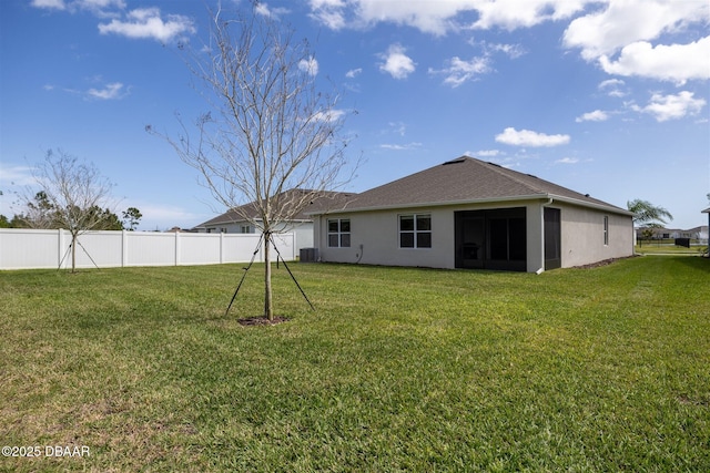 rear view of property featuring fence, a lawn, and stucco siding