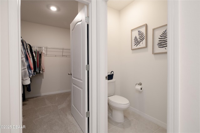 bathroom with tile patterned floors, a walk in closet, toilet, and baseboards