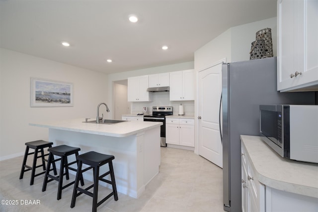 kitchen with a breakfast bar, appliances with stainless steel finishes, white cabinets, a sink, and under cabinet range hood